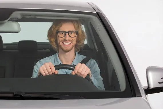 Lächelnder Fahrer sitzt angeschnallt am Steuer und blickt durch die Windschutzscheibe nach vorn.